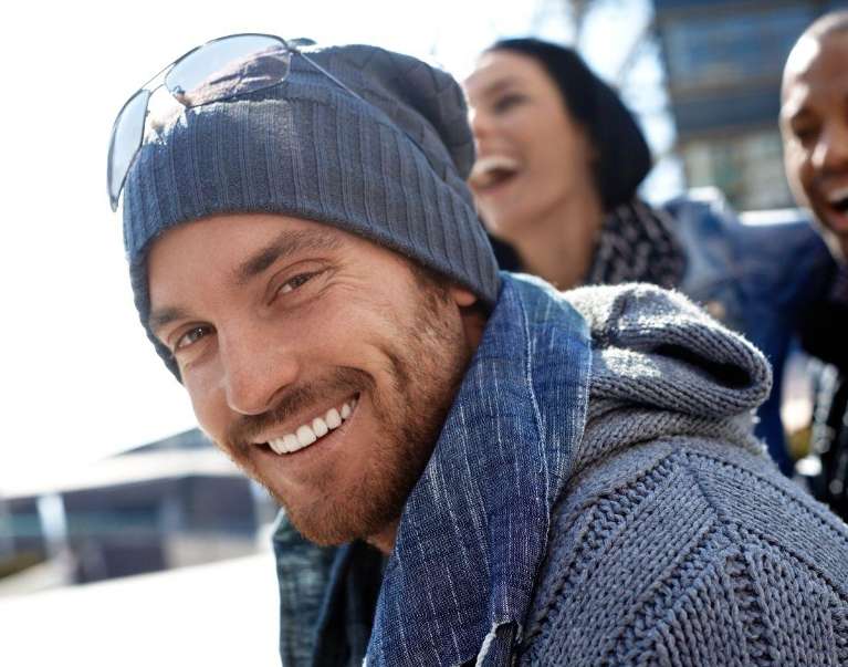 Smiling man in winter clothing showing healthy white teeth outdoors with friends
